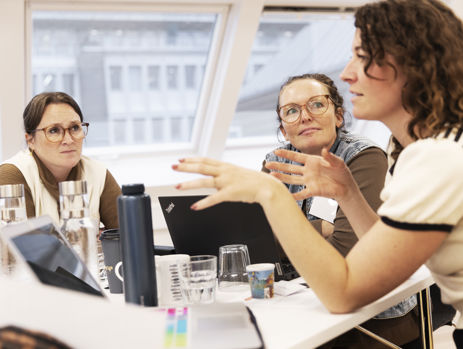 Tre gymnasielærere taler sammen ved et bord.