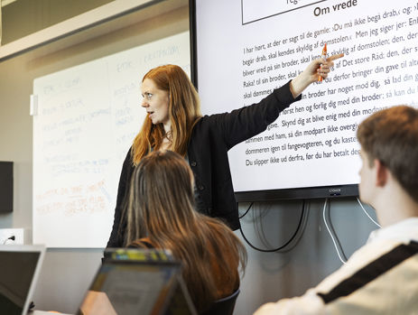 En gymnasielærer står og underviser en klasse foran et smartboard 