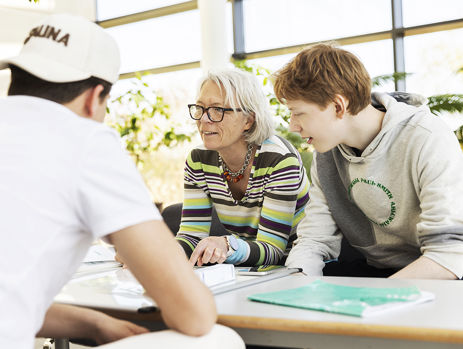 Gymnasielærer sidder ved et bord og taler med to elever