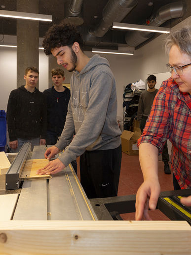 En gymnasielærer hjælper elever med at bruge en maskine i træværksted