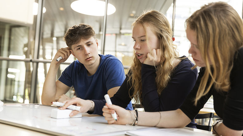 Tre elever sidder ved et bord og arbejder sammen om opgave 