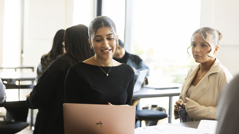 To elever sidder ved et bord og kigger på en computer sammen 
