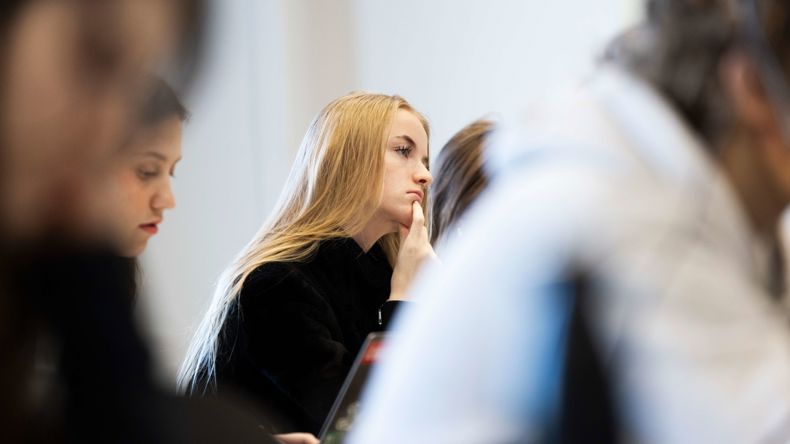 En elev sidder i et klasselokale og følger koncentreret med i undervisningen. Andre elever ses sløret i forgrunden.