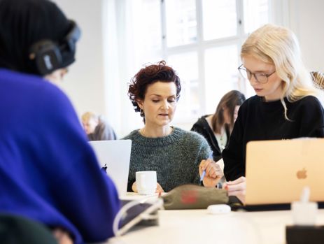 Gymnasielærer hjælper elev med en skriftlig opgave i klasselokalet.