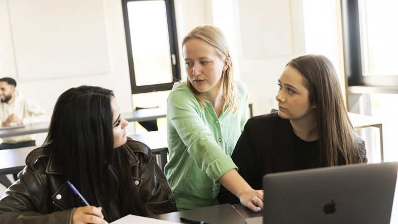 En gymnasielærer hjælper to elever i et klasselokale 