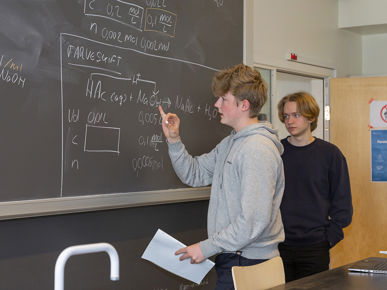 To elever står og løser opgaver oppe ved tavlen i klasselokalet